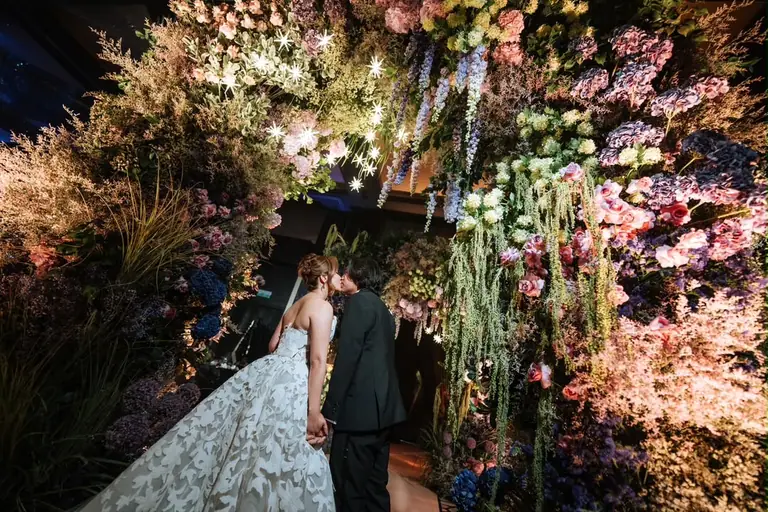 A couple together beneath a wall of flowers