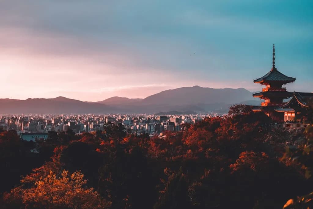 Kiyomizu-dera pagoda above autumn trees at sunset, looking over Kyoto city and the mountains